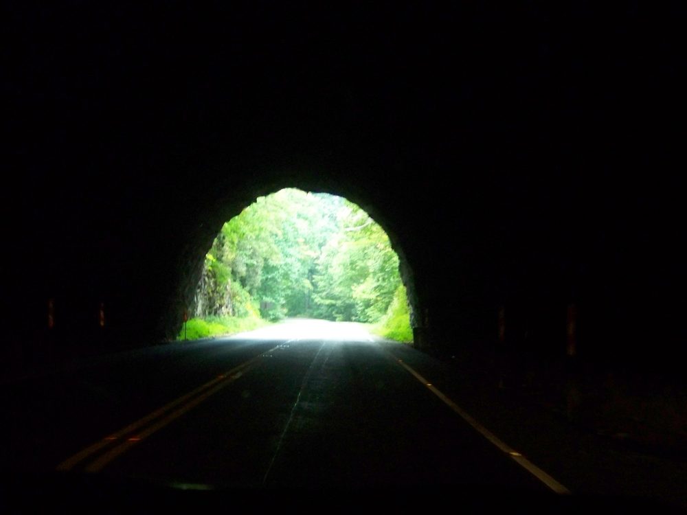 Looking out from a dark mountain tunnel toward sunlit green trees