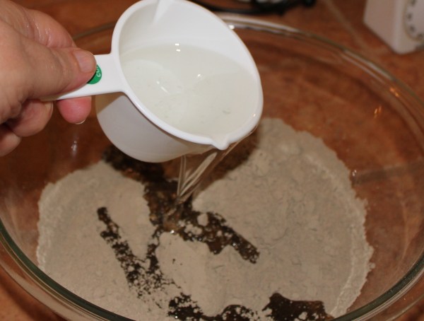 Melted coconut oil being poured into a bowl of powdered herbs