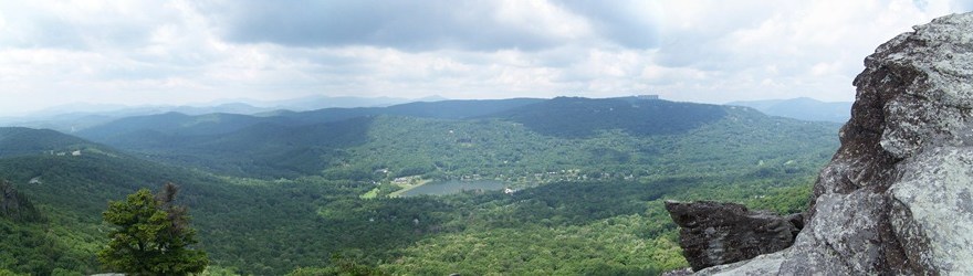 Panoramic view from Grandfather Mountain: ridge after ridge of the Blue Ridge fading into the distance above a green valley and lake